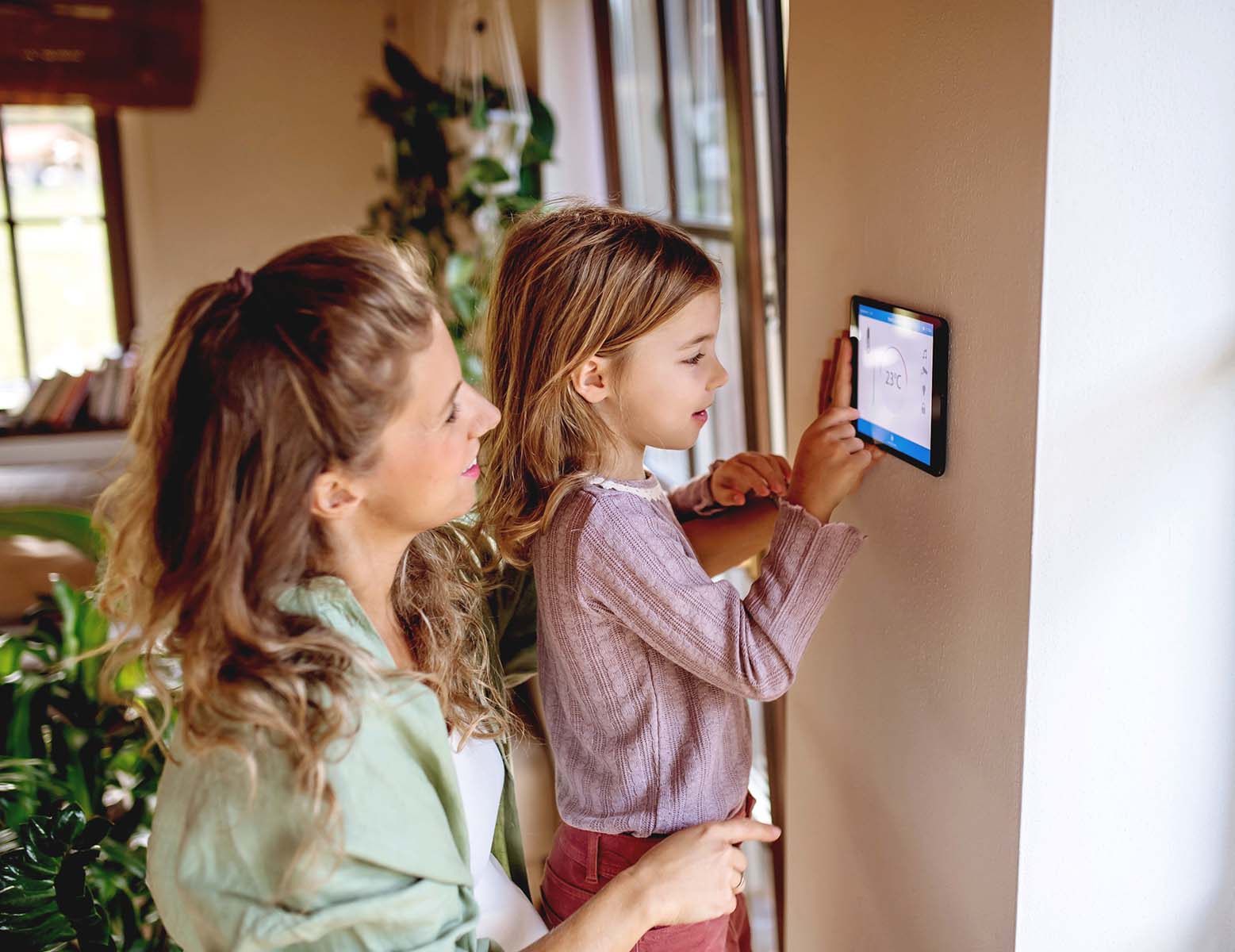 Woman and child adjusting a smart home thermostat.