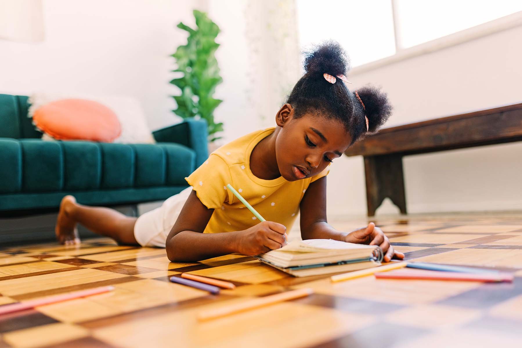 Child drawing on the floor with colored pencils.
