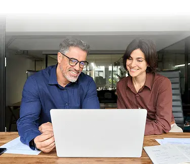 Man and woman smiling while sitting at a desk looking at a laptop