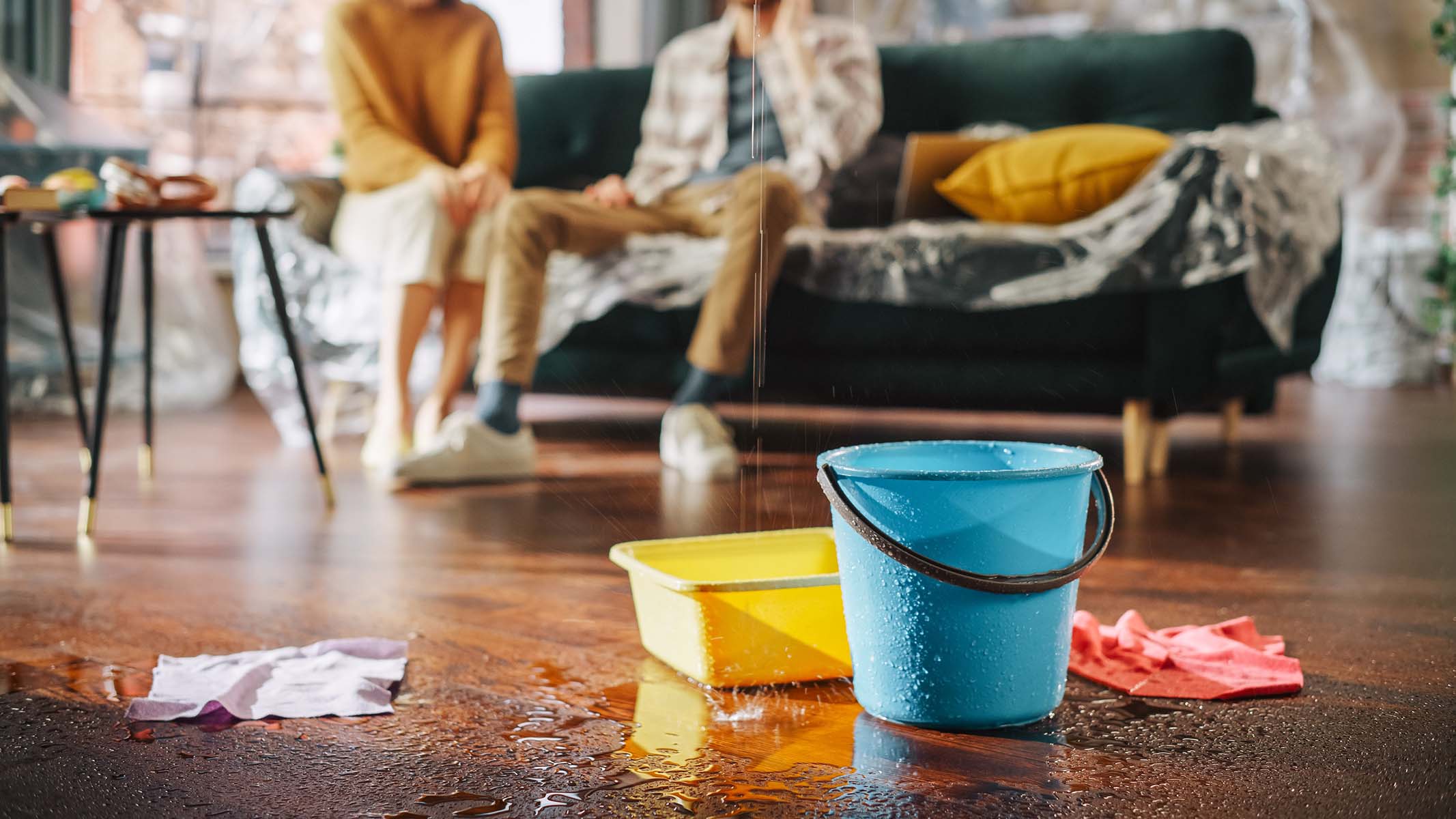 Buckets catch a leak on a wet floor with two people in the background.