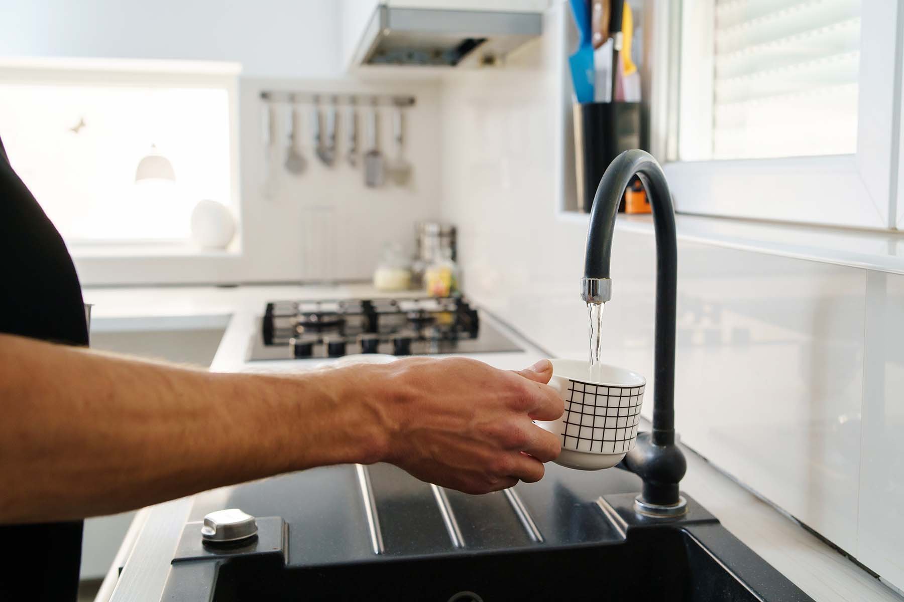 A person fills a patterned cup with water from a kitchen tap