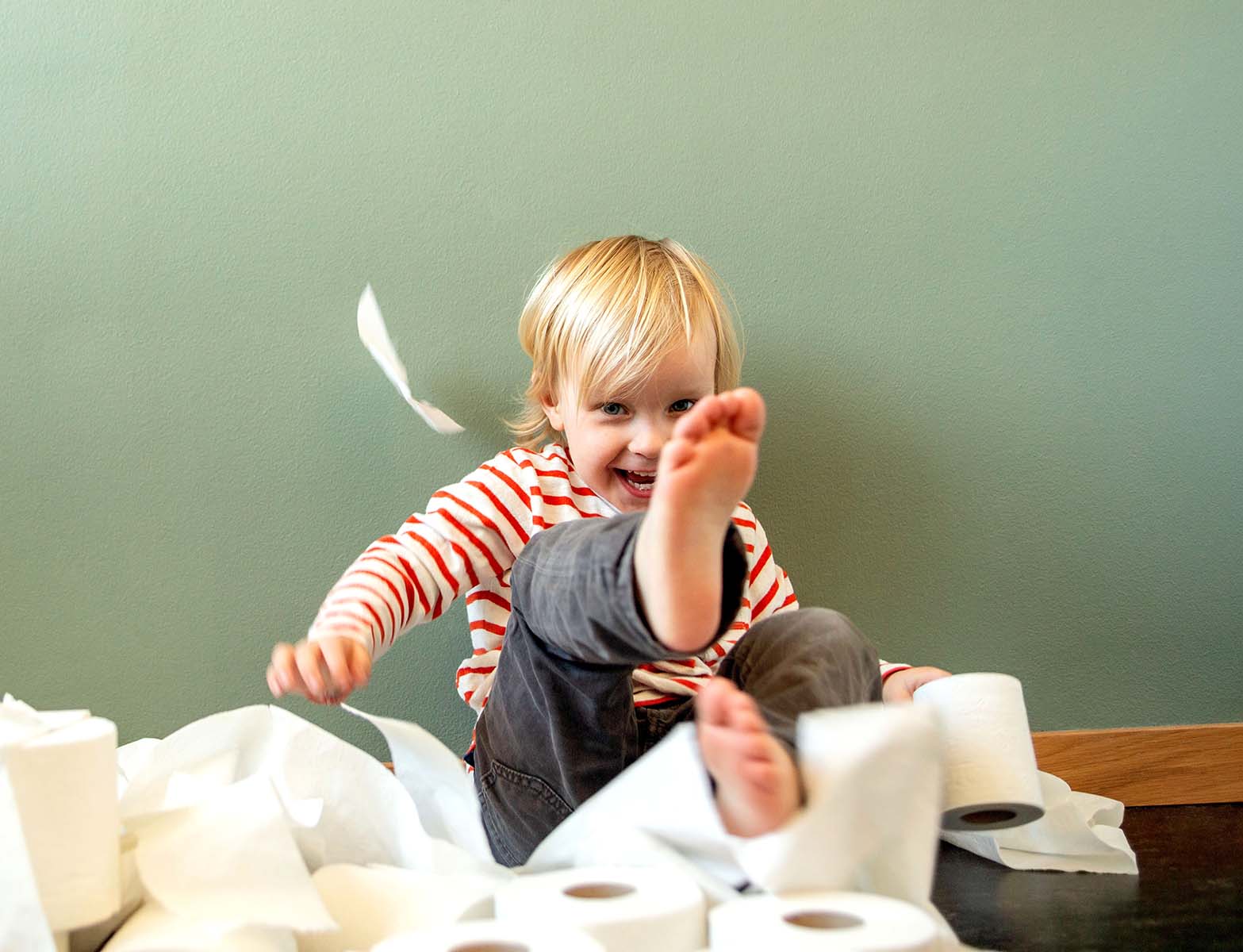 A toddler gleefully throwing toilet paper around.