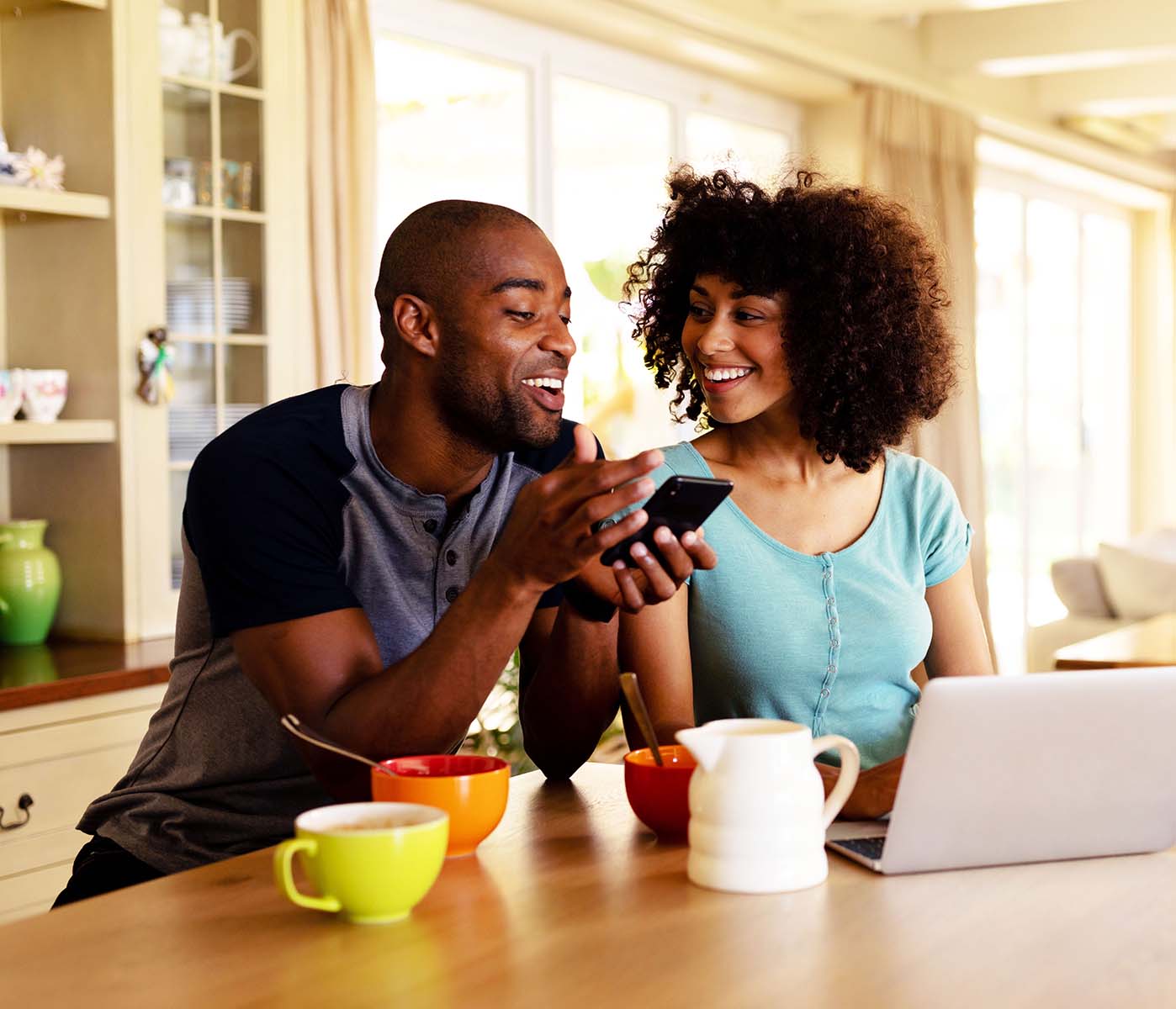 Couple looking at a smartphone with coffee and a laptop on the table.