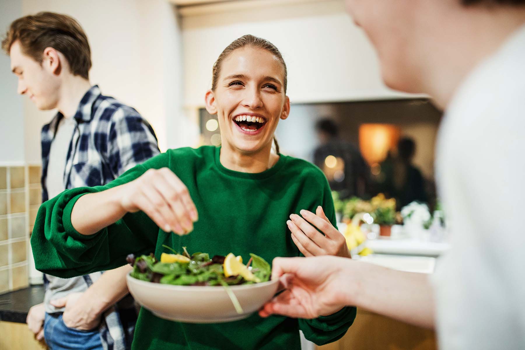 Laughing woman serving salad with people in the background.