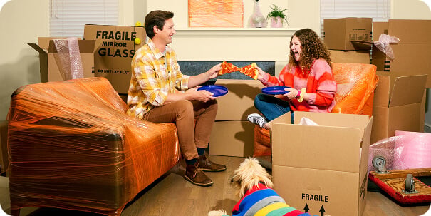 A couple wearing brightly colored clothes are sitting in a brightly colored room unpacking moving boxes.