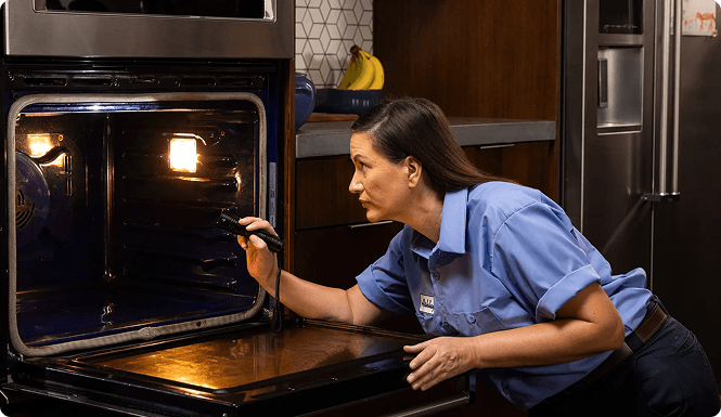 Expert inspecting inside of oven with flashlight