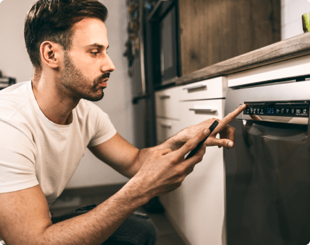 Man looking at phone while pressing dishwasher buttons